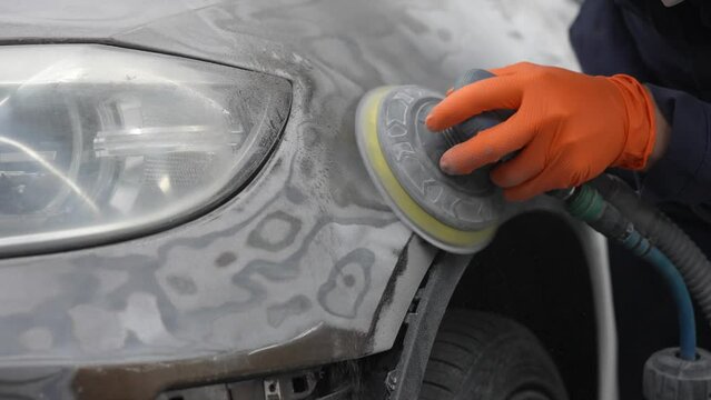 A mechanic sands the putty on a car body with a machine. Repair after an accident. 