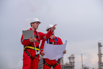 Engineer wear uniform and helmet stand workplace hand holding tablet computer, survey inspection team work see detail blue print plant site to work with oil refinery  background. - 800795686