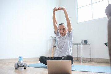 Senior Healthy Man Stretching Hands, Warming Up Before Workout at Yoga Mat with Online Instructor at Home 