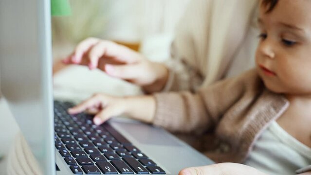 Pretty young single mom working at home on a laptop computer while holding her baby girl 