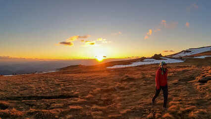 Silhouette of woman walking on alpine pasture towards sunset on mountain peak Ladinger Spitz,...