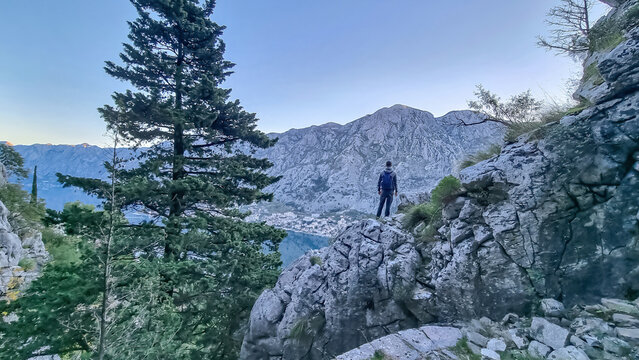 Rear view of man with backpack on rock looking at scenic view near Vrmac Sveti Ilija in summer, Adriatic Mediterranean Sea, Montenegro, Balkans, Europe. Hiking trail in Kotor bay, Dinaric Alps