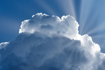 Bright sun rays coming out from thick clouds of a summer sky