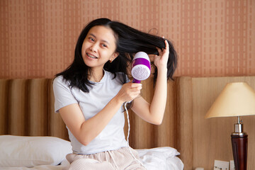 Woman sitting on bed blow drying hair
