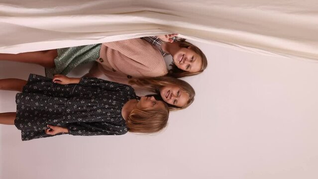 Three girls peek out from behind a curtain against a white wall. Concept: family bonding, child development ads, copy space.