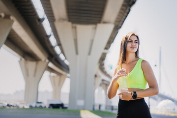 Fitness woman with a drink, modern bridge, daylight.