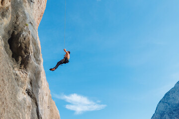 rock climber descends from a route, a climber hangs on a rope against the sky. © zhukovvvlad