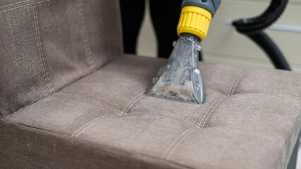 Woman cleaning a fabric chair with a professional washing vacuum cleaner. 