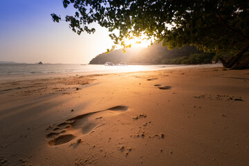 Golden sunset over a tranquil beach, with footprints leading towards the sea