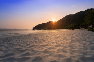 Serene sunset view over a sandy beach with clear skies and lush hills