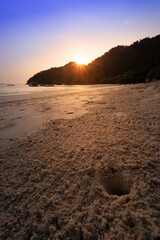 Golden sunset peering over a calm beach with intricate sand patterns