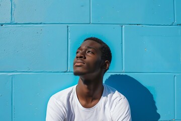 Depict a pensive African American male college attendee gazing upwards at the brilliant cerulean expanse while seated crosslegged on sundappled ground