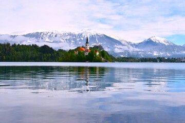 View of the church on island at Bled lake in Gorenjska, Slovenia with Karavanke mountains covered in snow in the background