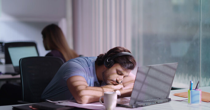 Indian Asian youth tense tired sad business man agent boy siting chair use laptop indoor job office need nap lack sleep feel bad drowsy lazy sleep closed eyes young adult bored upset gen z male staff