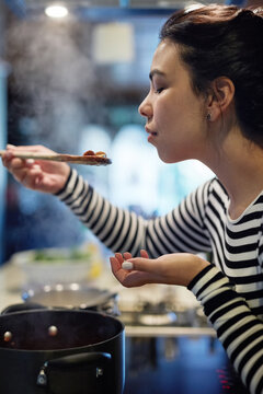 Woman, cooking and food with taste in kitchen for flavor, test and evaluation of ingredients. Home, nutrition and female person with spoon in hand for dinner, preparation and assessment of recipe