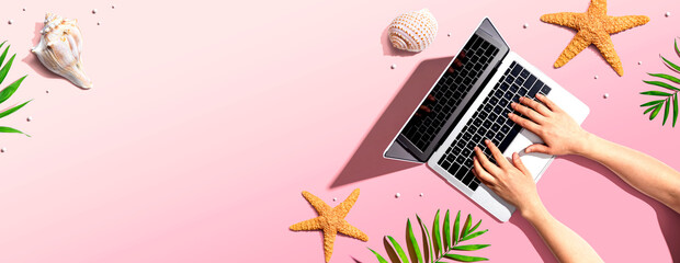 Person using a laptop computer with summer theme objects - flat lay