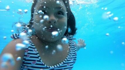 Adorable young girl swims underwater with a joyful expression, surrounded by bubbles