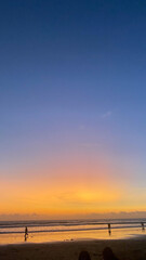beautiful orange sunset with people on the beach and a pink, purple and blue sky.