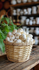A wicker basket filled with fresh garlic bulbs on a wooden table, with shelves of pottery blurred in the background.