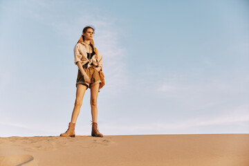Woman standing confidently on top of sand dune with hands on hips in majestic desert landscape