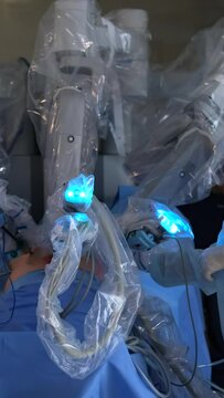 Robotic surgery in a sterile environment. A nurse supervises a multi-armed robot performing a surgical procedure. Medical equipment and monitors in the foreground.