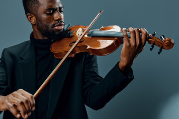 Elegant African American musician playing violin in black suit on neutral gray background, music...