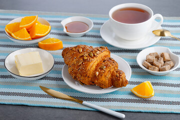 Fresh croissant with butter and tea, orange for breakfast