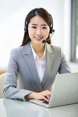A korean woman in a grey blazer sits at a desk with a laptop and a headset on. She looks into the camera with a smile. AI Generative