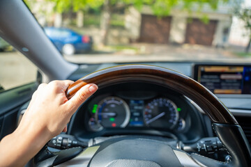 View of a woman's hand on the steering wheel of a car while driving in the city