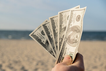 Unrecognizable woman Displaying Spread of Cash dollars bills on sandy beach coastline. Concept...