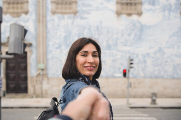 Tourist standing holding hands with scarf and backpack smiling looking at camera near church with famous Portuguese blue ceramic tiles. Honeymoon.