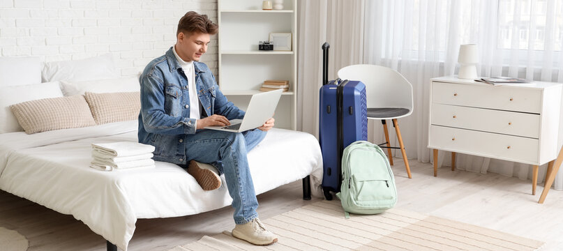 Male tourist using laptop on bed in hotel room - Powered by Adobe