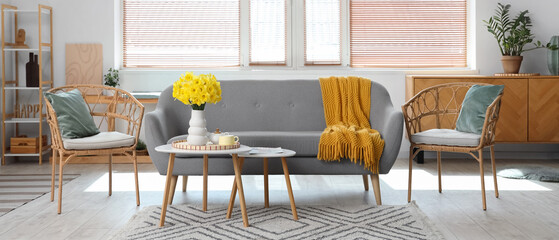 Interior of living room with grey sofa, carpet, coffee tables and vase of narcissus flowers