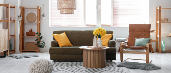 Stylish interior of living room with cozy sofa, coffee table and bouquet of narcissus flowers