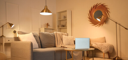 Interior of cozy living room with sofa and laptop on table in evening