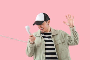 Stressed young man talking by phone on pink background