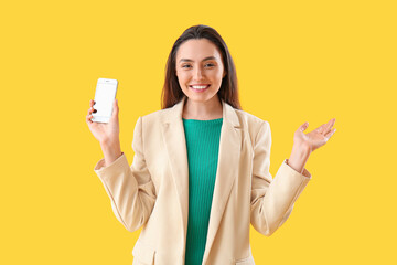 Happy young woman with smartphone on yellow background