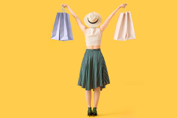 Beautiful young woman with shopping bags on yellow background, back view