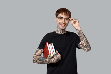 Young tattooed man with books on grey background