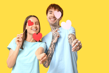 Funny young couple with paper hearts on yellow background