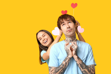Funny young couple with paper hearts on yellow background
