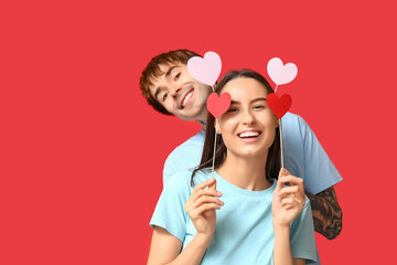 Funny young couple with paper hearts on red background