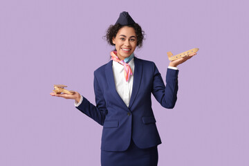 Beautiful African-American stewardess with toy planes on lilac background