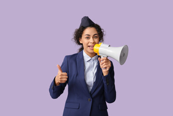 Beautiful African-American stewardess with megaphone showing thumb-up on lilac background