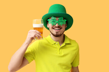Happy young man in leprechaun's hat with glass of beer on yellow background. St. Patrick's Day...