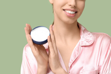 Beautiful young woman with jar of face cream against green background