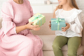 Young woman with her cute little daughter holding gift boxes and sitting on sofa at home, closeup