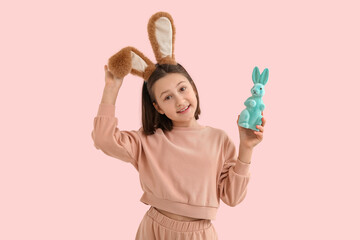 Happy little girl in Easter bunny ears with toy rabbit on pink background