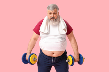 Overweight mature man with dumbbells on pink background. Weight loss concept