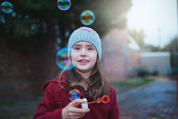 Child, happy and blowing bubbles for outdoor playing with holiday fun in winter, childhood or development. Girl, kid and smiling outside in cold weather as preschool student, joyful or positivity